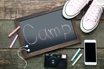 Inscription Camp with smartphone, retro camera and sport shoes on wooden table