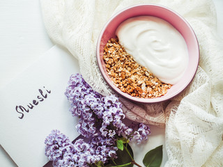 Smoothies, muesli with nuts in a beautiful plate, napkin, bouquet of blooming lilacs and notebook with an inscription on a white table. Top view, close-up. Сoncept of healthy nutrition and longevity