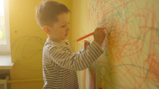 little boy drawing on the yellow wall at home
