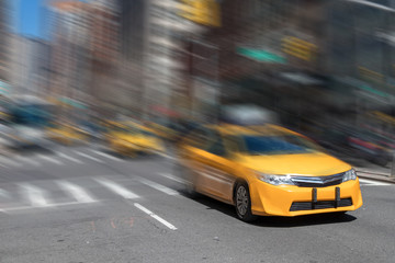 Fototapeta na wymiar Fast paced yellow taxi cab driving through Manhattan streets in New York City with motion blur background