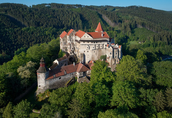 Fototapeta na wymiar Moravian castle Pernstejn, standing on a hill above deep forests of the Bohemian-Moravian Highlands against blue sky. Aerial photography. Ancient royal castle in Czech landscape, czech travel place.