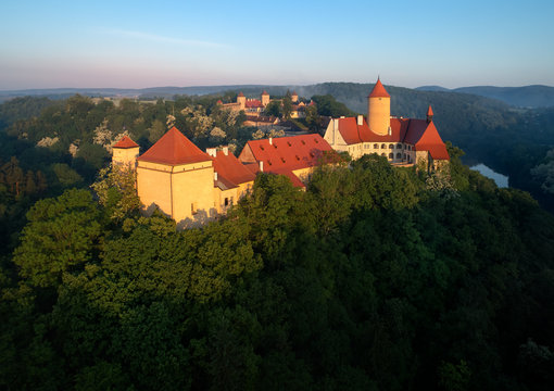 Aerial view of beautiful, Moravian royal castle Veveri or Burg Eichhorn, standing on a rock above water dam on river Svratka. Large castle above misty trees in early morning light. Aerial photography.