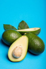 Fresh organic ripe green whole and sliced Fuerte avocado with leaves, copy space close up isolated on trendy blue background