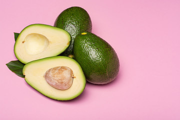 Fresh organic ripe green whole and sliced Fuerte avocado with leaves, copy space close up isolated on trendy pink background