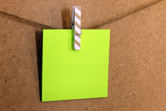 Hoja de papel de color verde  (posit), sujeto con una peque&ntilde;a pinza de colore rosa con puntitos blancos, en una cuerda a la pared de corcho. 