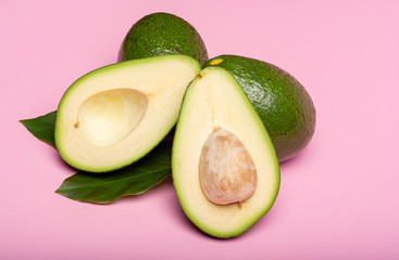 Fresh organic ripe green whole and sliced Fuerte avocado with leaves, copy space close up isolated on trendy pink background