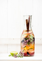 Summer lemonade with berries, herbs and fruits in a glass bottle on a white wooden background