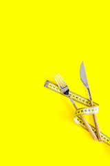 Diet, weight loss, slimming concept. Fork and knife with wound measuring tape on yellow background...