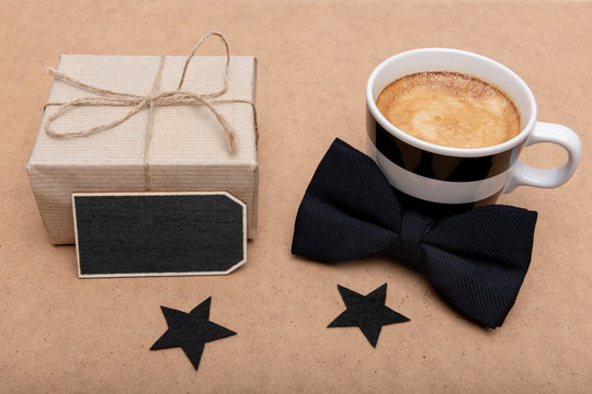 Happy Father's Day Background. Cup of coffee, beautiful present and black bow tie on brown background flat lay. Fathers day still life setup. - Powered by Adobe