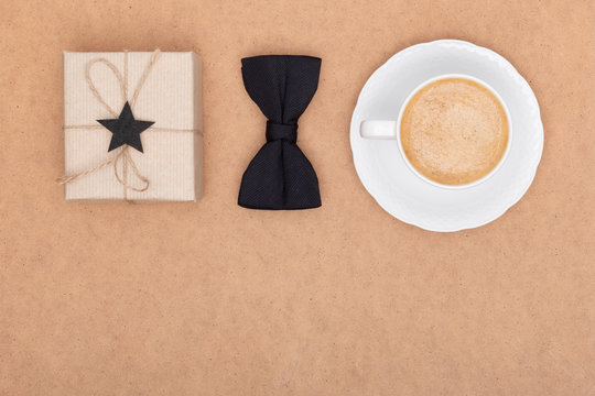 Happy Father's Day Background. Cup of coffee, beautiful present and black bow tie on brown background flat lay. Fathers day still life setup. - Powered by Adobe
