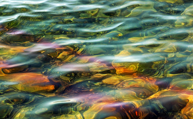 Fototapeta na wymiar Beautiful waters with soft ripples on surface. Rocks can be seen on shallow bottom below 