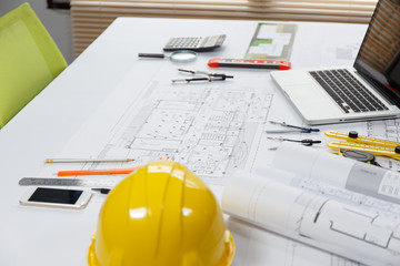 Blueprints, helmet, laptop, pencil, dividers, smartphone and engineer equipment on working desk.