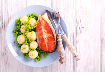 Fried trout steak and young potatoes with peas on plate