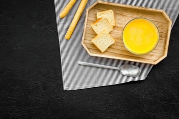 Pumpkin cream soup ready to eat served with rusks on black background top view copy space