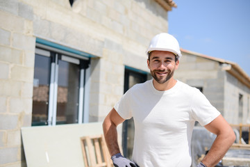 portrait of handsome construction worker on a house building industry construction site - obrazy, fototapety, plakaty