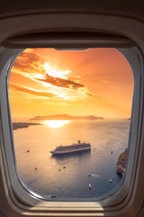 Amazing evening view of Fira, caldera, volcano of Santorini, Greece with cruise ships at sunset through a frame of plane window.