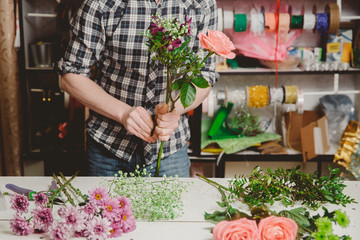 Man florist collects modern bouquet of pink roses, is dressed in plaid shirt. Concept gift for woman.