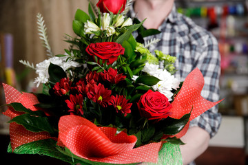 Workplace florist, man collects modern bouquet of hands of roses and white chrysanthemums, holds in hands