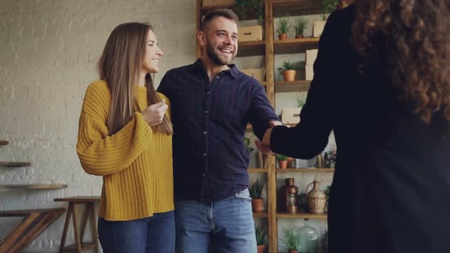 Slow motion of real estate buyers getting keys from housing agent after successful deal, kissing and hugging with happiness and shaking hands to female broker.