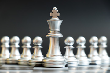 Silver king chess piece stand in front of pawn on black background (Concept of leadership, management)