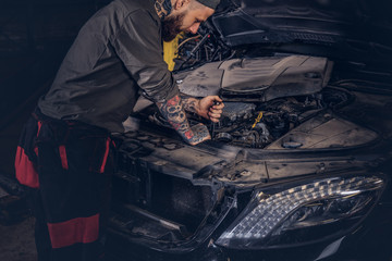Naklejka na ściany i meble Auto mechanic checks the car engine during repair in a garage.