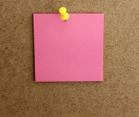 Hoja de papel cuadrada de color rosa, posit, clavado con una chincheta amarilla, en la pared...
