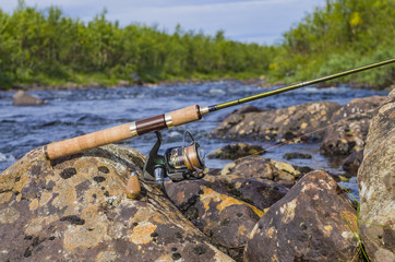 Fishing spinning rod with reel on river stones