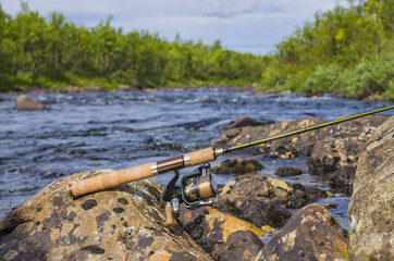 Fototapeta na wymiar Fishing spinning rod with reel on river stones