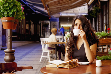 Pretty young woman is resting in cafe terrace and reading book during her free time before works. Success, freelancer, relax, education concept.