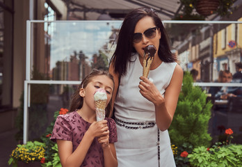 Fashionable mother and cute daughter enjoy ice cream on a hot summer day.