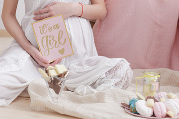 pregnancy woman in white dress sitting on the floor at the celebration baby shower party.she holds a postcard with the inscription "this is a girl".pregnancy, motherhood concept