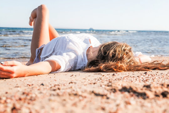 Young adult tanned blond girl lies on the sand on the beach near the sea and smiles.