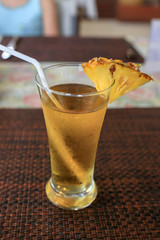 Pineapple juice in a glass with drinking straw and a piece of pineapple.