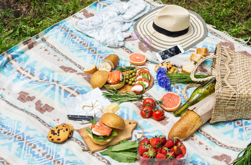 Picnic setting on the grass with basket, sandwiches, fruit, strawberry, salad and olives