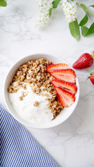 Perfect breakfast: crunchy granola with yoghurt and strawberries with a cup of black coffee on marble table