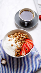 Perfect breakfast: crunchy granola with yoghurt and strawberries with a cup of black coffee on marble table