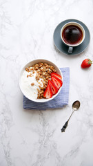 Perfect breakfast: crunchy granola with yoghurt and strawberries with a cup of black coffee on marble table