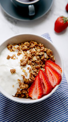 Perfect breakfast: crunchy granola with yoghurt and strawberries with a cup of black coffee on marble table