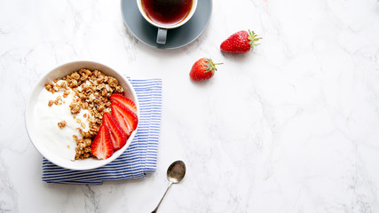Obraz na płótnie Canvas Perfect breakfast: crunchy granola with yoghurt and strawberries with a cup of black coffee on marble table. Flat lay with copy space
