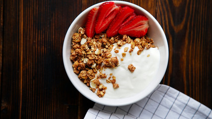 Perfect breakfast: crunchy granola with yoghurt and strawberries with a cup of black coffee on wooden table. Close up top view.