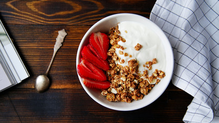 Fototapeta premium Perfect breakfast: crunchy granola with yoghurt and strawberries with a cup of black coffee on wooden table. Close up top view.