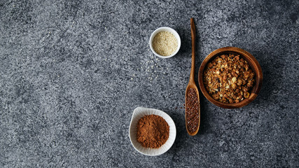 Healthy sweets cooking ingredients: granola, sesame and flax seeds, cocoa in separate bowls on gray background. Flatlay with copy space