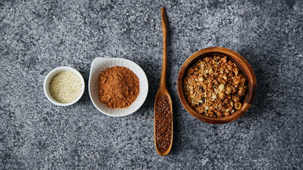 Healthy sweets cooking ingredients: granola, sesame and flax seeds, cocoa in separate bowls on gray background. Flatlay with copy space