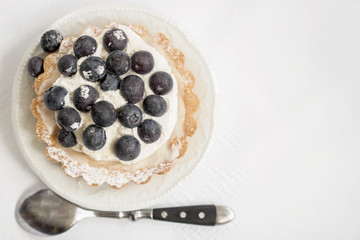 Fresh blueberry tart in portion plate, next to a spoon, white napkin. Delicious summer berry dessert. Top view, copy space for text, background