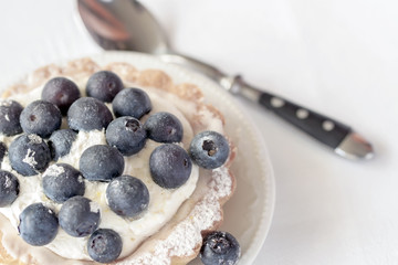 Fresh blueberry tart in portion plate close-up and spoon, white napkin. Delicious summer berry dessert. Top view