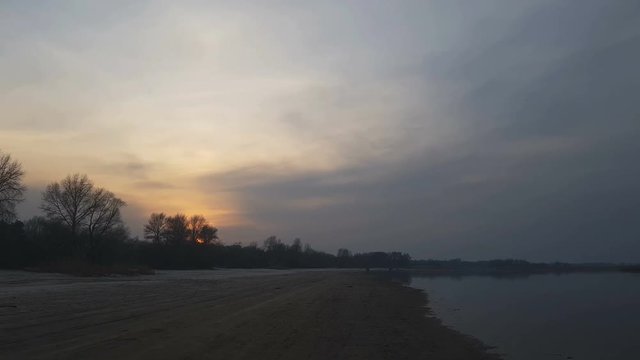 Sunset on the river bank. The Red Sun goes beyond the horizon on the beach. Beautiful spring evening.