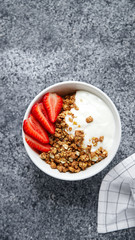 Perfect breakfast: crunchy granola with yoghurt and strawberries with a cup of black coffee on gray bakcground. Flat lay with copy space