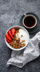 Perfect breakfast: crunchy granola with yoghurt and strawberries with a cup of black coffee on gray bakcground. Flat lay with copy space