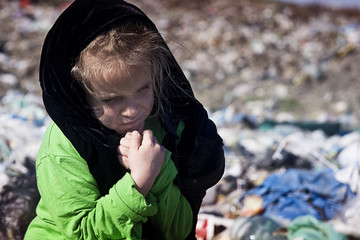 A poor child is warming his hands in a garbage dump