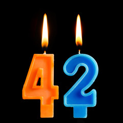 Burning birthday candles in the form of 42 forty two for cake isolated on black background.